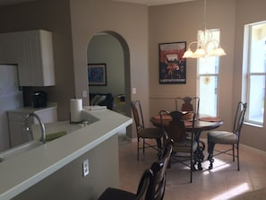 A modern kitchen with a central island, dining table, and chairs. There is a poster on the wall and a window providing natural light. - Endless Summer, Gorgeous Sunsets! Spacious Lakefront 4/3 with pool and spa! (Fort Myers)