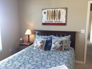 A bedroom with a bed, pillows, a nightstand, a lamp, and a wall hanging. - Endless Summer, Gorgeous Sunsets! Spacious Lakefront 4/3 with pool and spa! (Fort Myers)