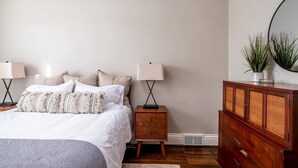 Un dormitorio con una cama, dos mesitas de noche con lámparas, un aparador de madera y un espejo en la pared.