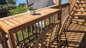A wooden deck with a potted plant, wicker chairs, and a view of the water and buildings in the background.