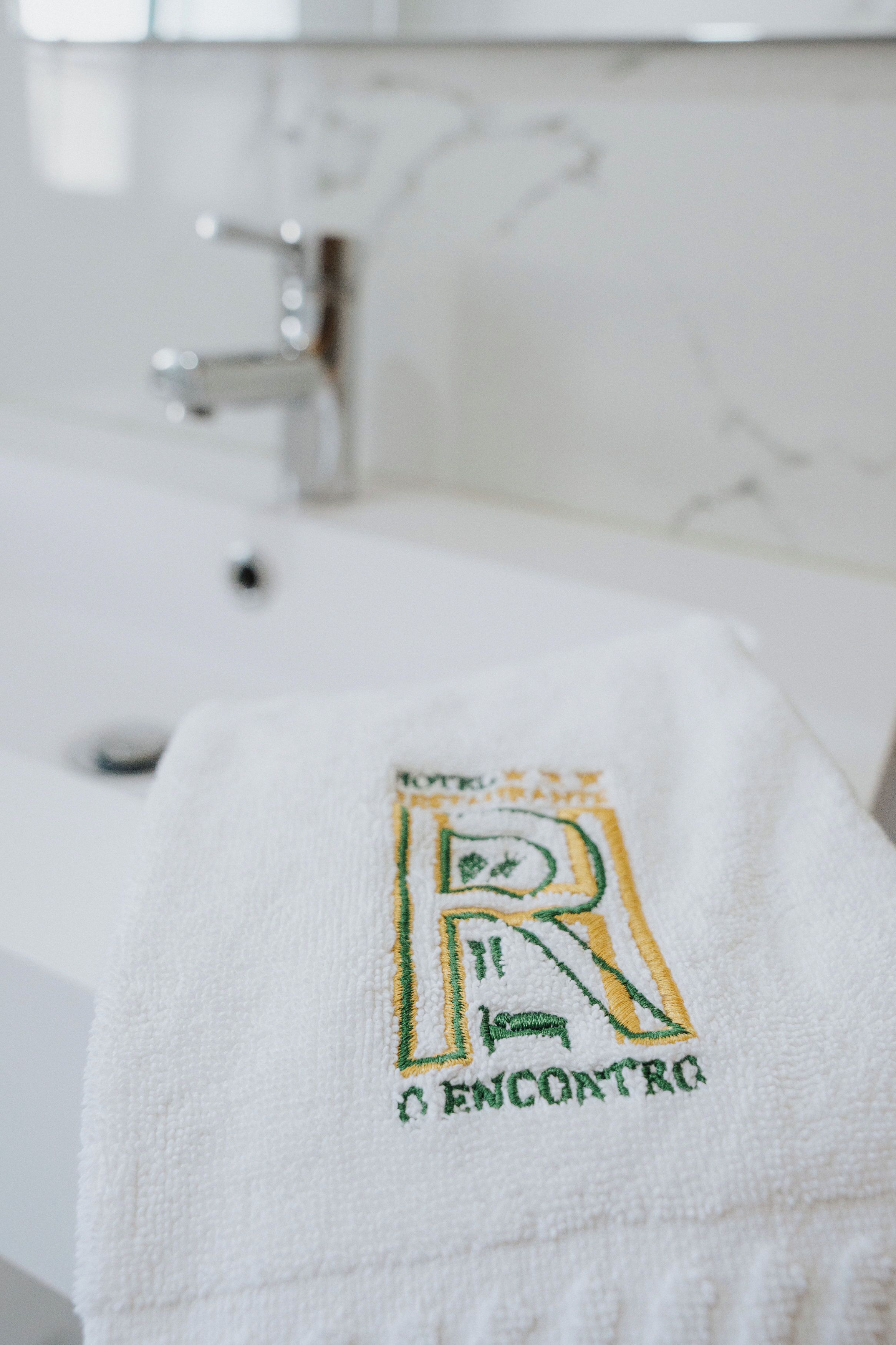 Una toalla blanca con texto bordado y un logotipo sobre un lavamanos de baño.