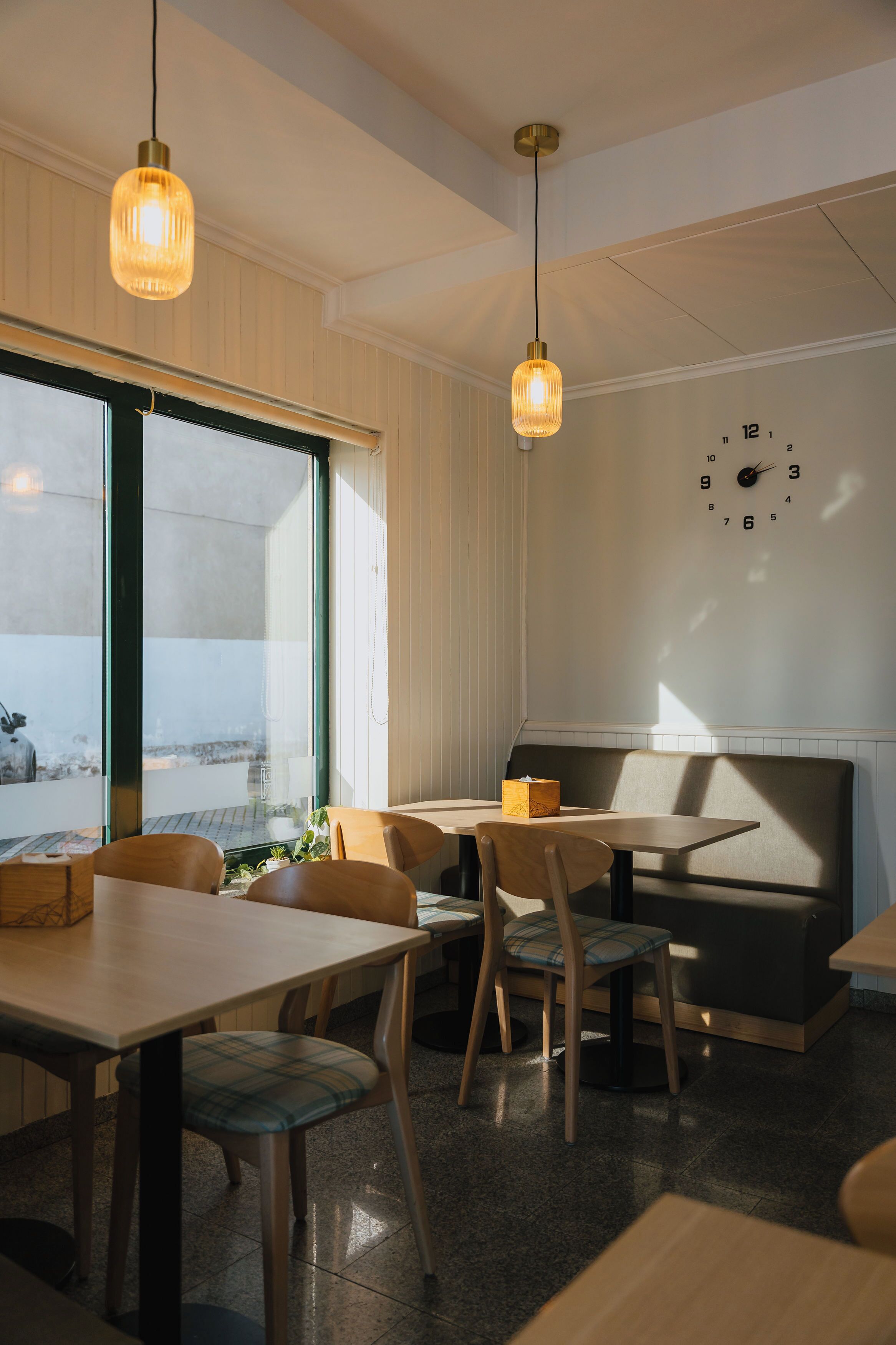 A modern dining area with wooden tables and chairs, a bench, and pendant lighting.