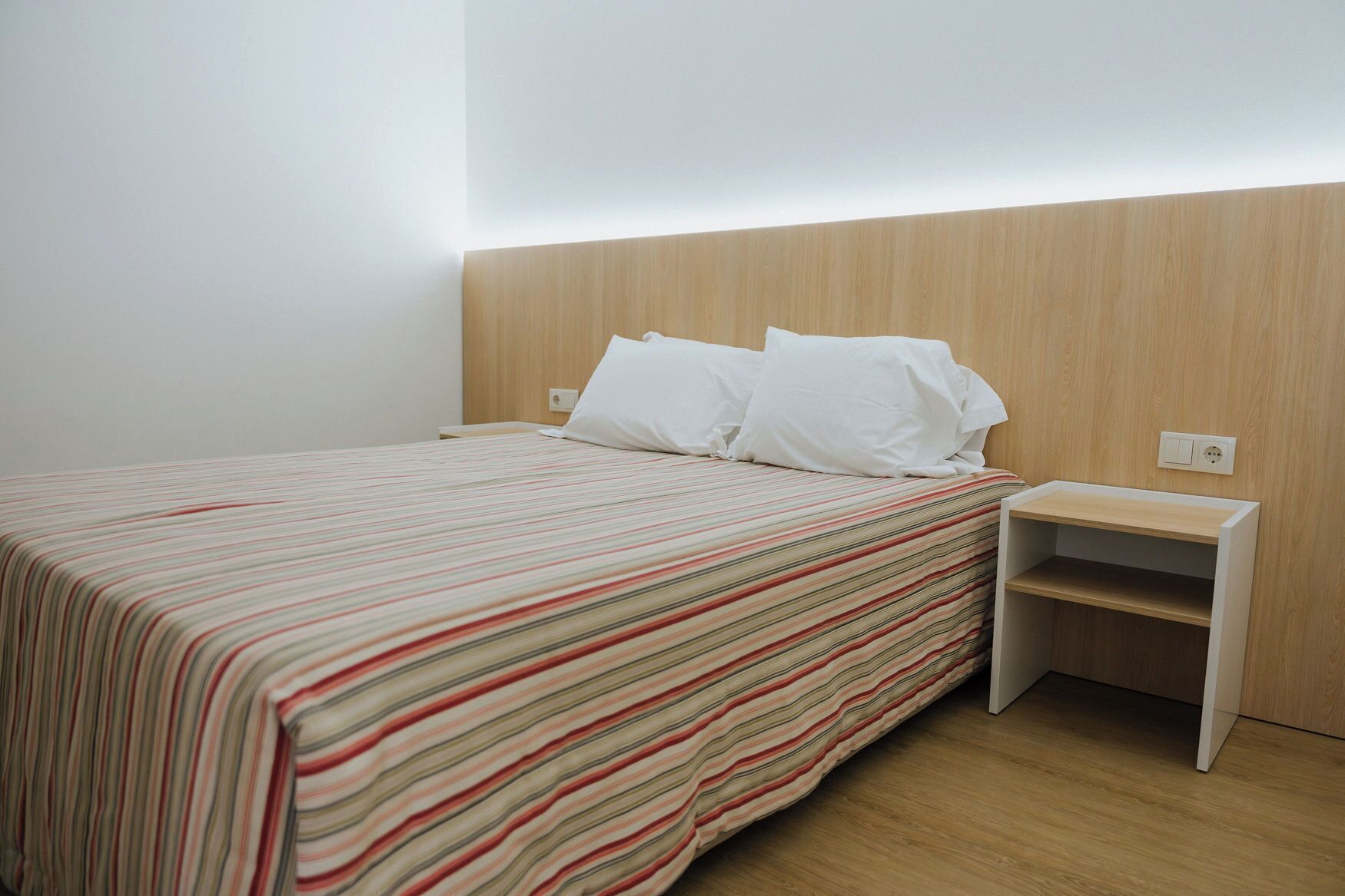 A neatly made bed with a striped bedspread, a wooden headboard, and a bedside table with a shelf.