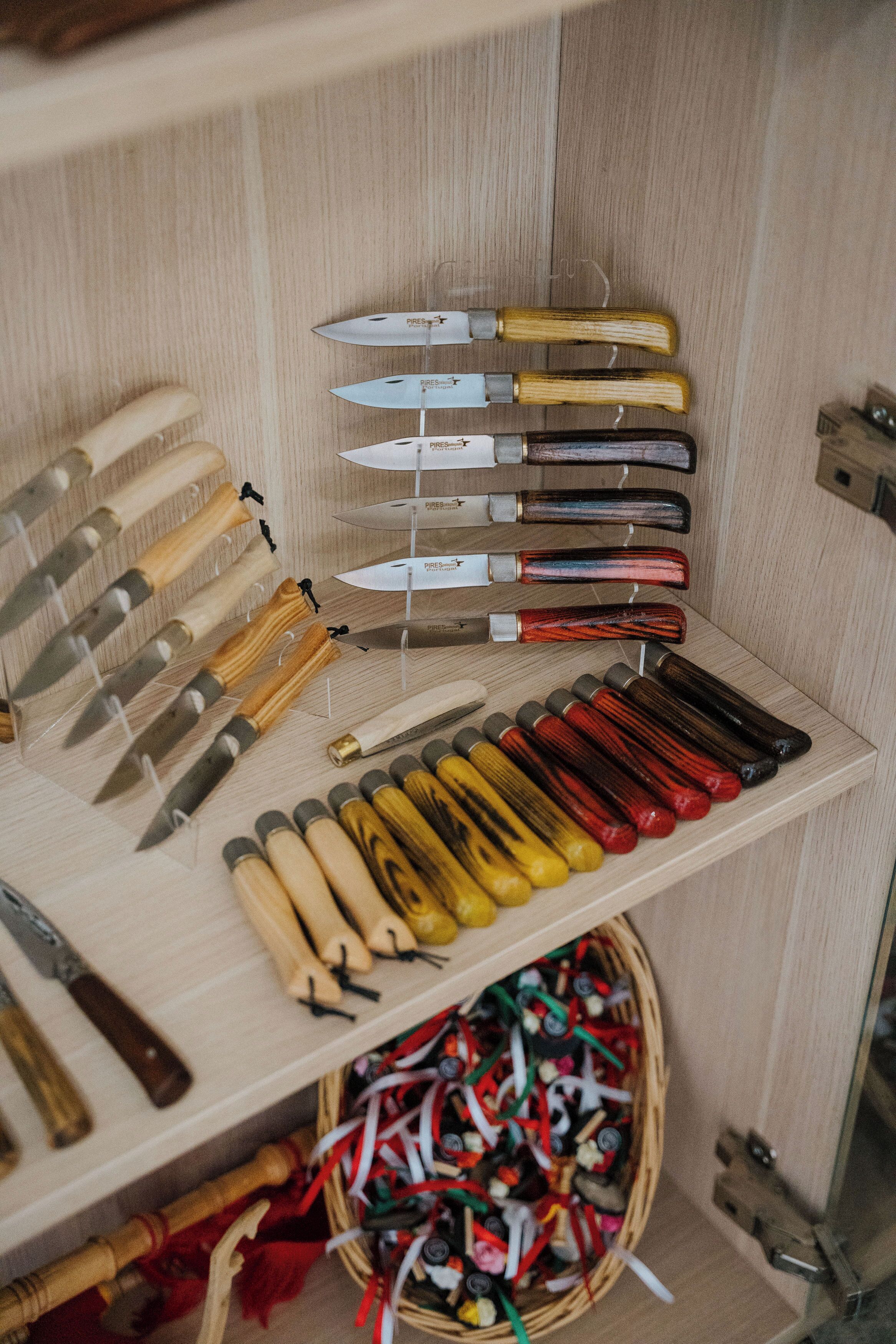 A display of various knives with wooden handles, arranged on shelves and a wooden rack.