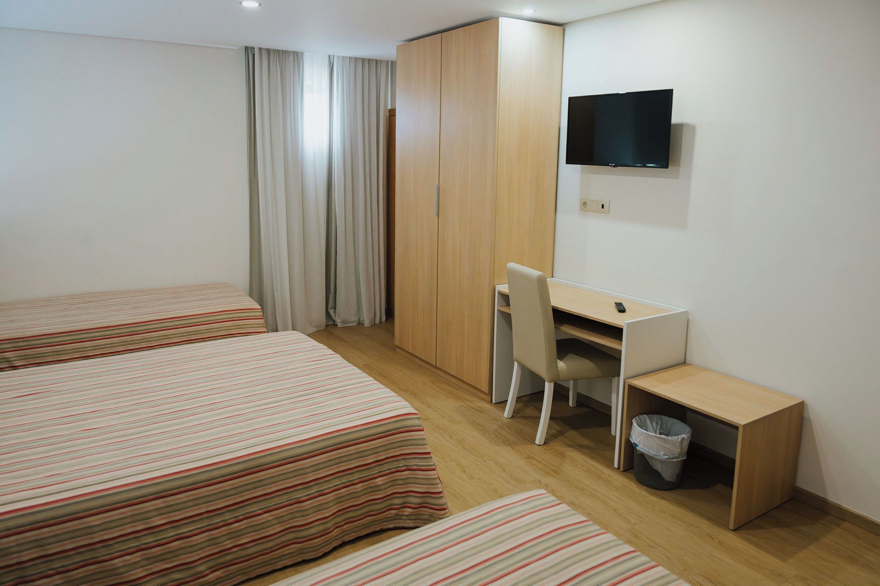 A hotel room with two beds, a desk, a chair, a TV, and a wardrobe.
