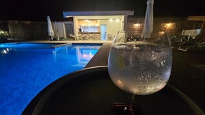 A swimming pool with lounge chairs and umbrellas, a glass of water, and a building with a bar in the background. - Hotel O Encontro (Miranda do Douro)