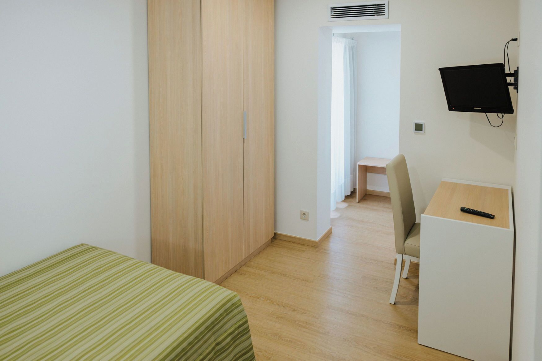 A small, clean room with a bed, a desk, and a TV.