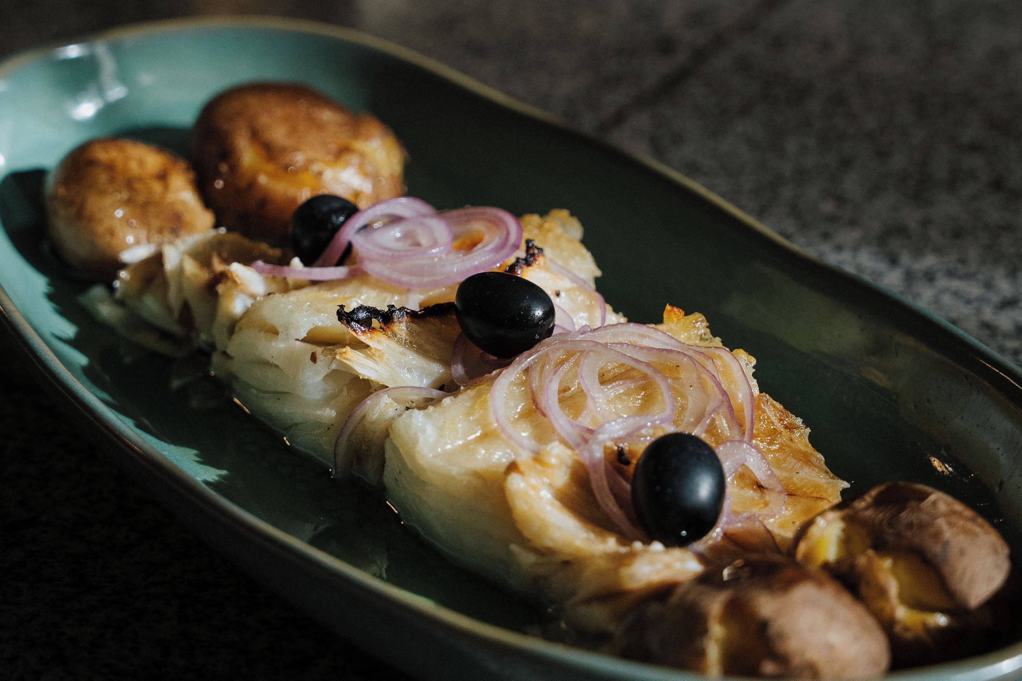 Un plat composé de poisson, d’olives et d’oignons, servi dans une assiette.