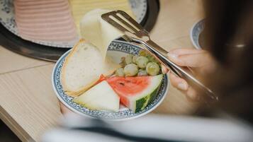 Un comedor con un plato de carne en rodajas, un bol de fruta y una tabla de queso.