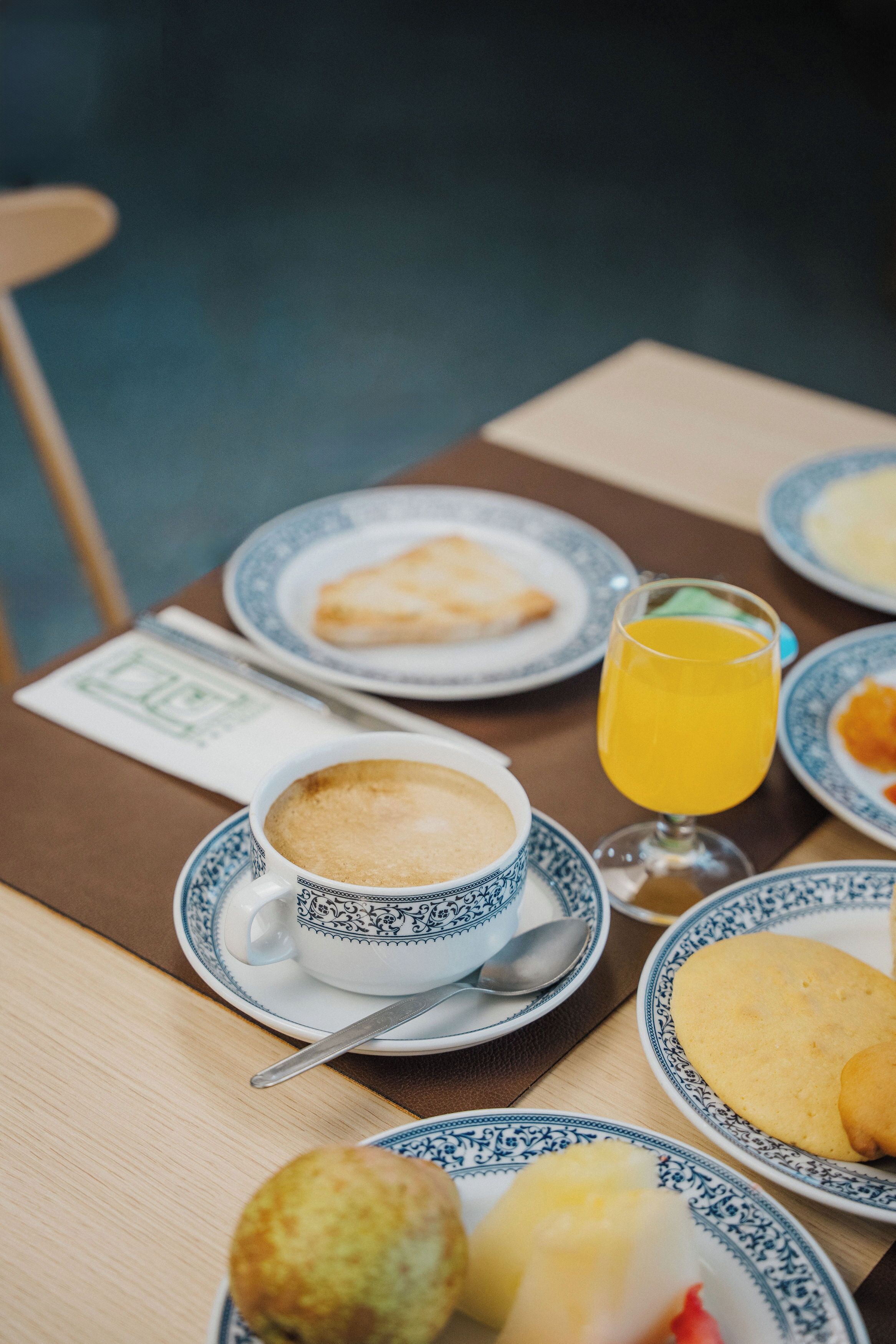 Una mesa de desayuno con una taza de café, un vaso de zumo de naranja y platos de comida.