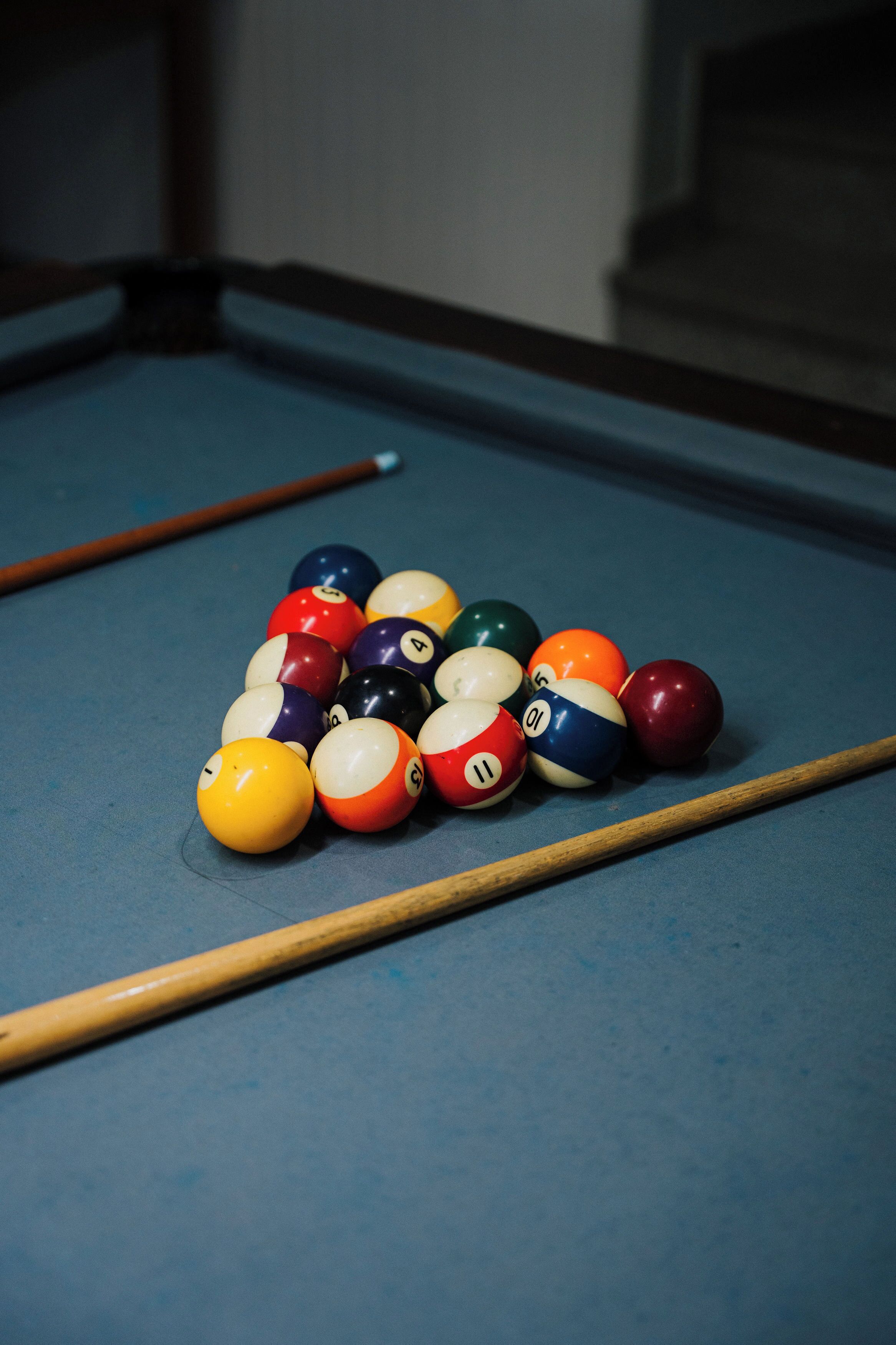 A pool table with a set of billiard balls and two pool cues.