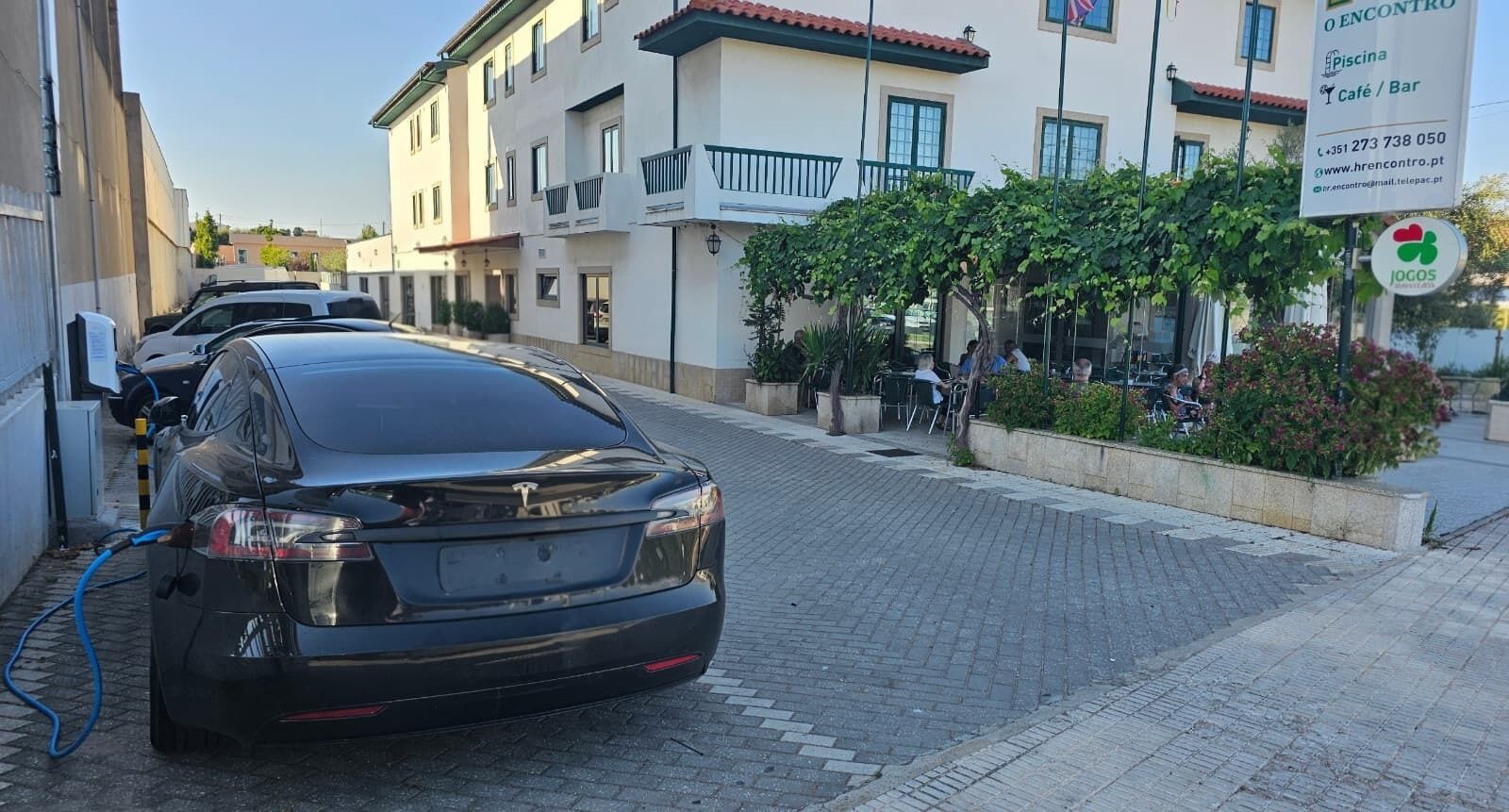 Un coche negro estacionado en una calle pavimentada, con un edificio al fondo.