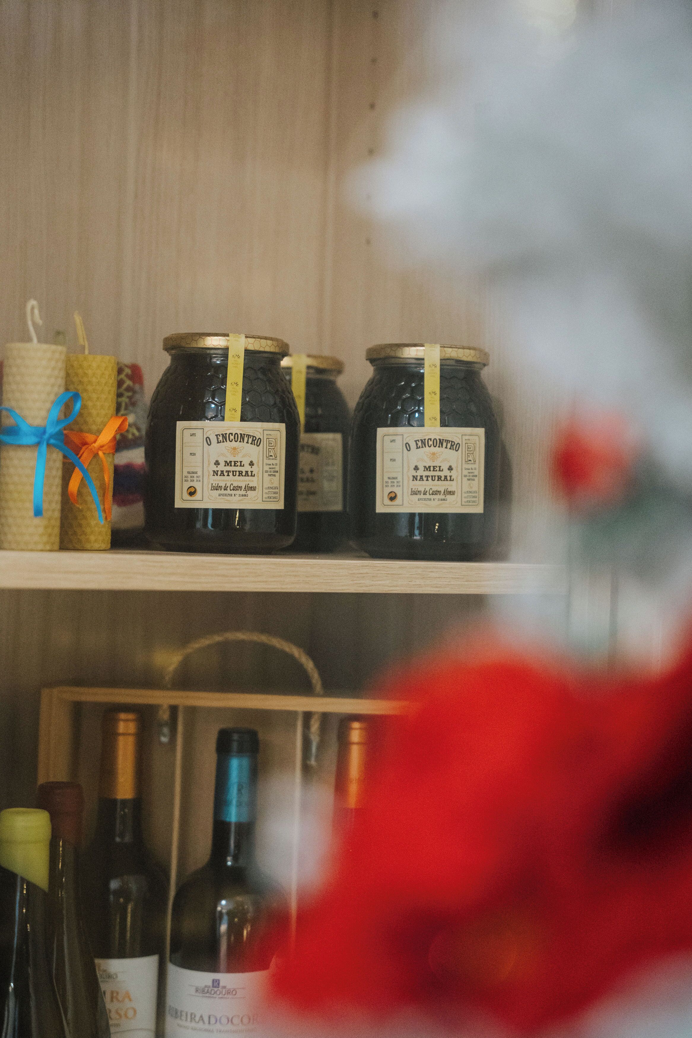 A shelf with jars labeled "O ENCONTRO MEL NATURAL" and a bottle of wine.
