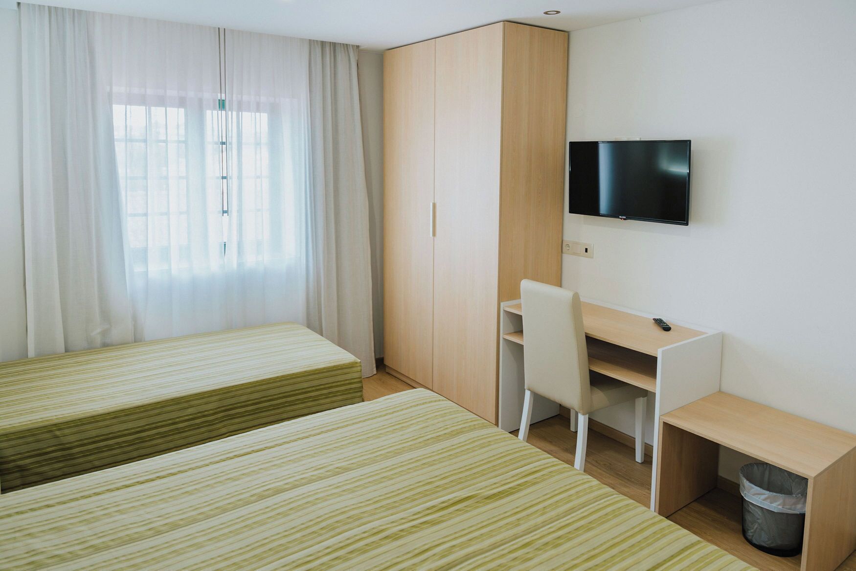 Une chambre d’hôtel avec deux lits simples, un bureau avec une chaise, une télévision et une armoire.