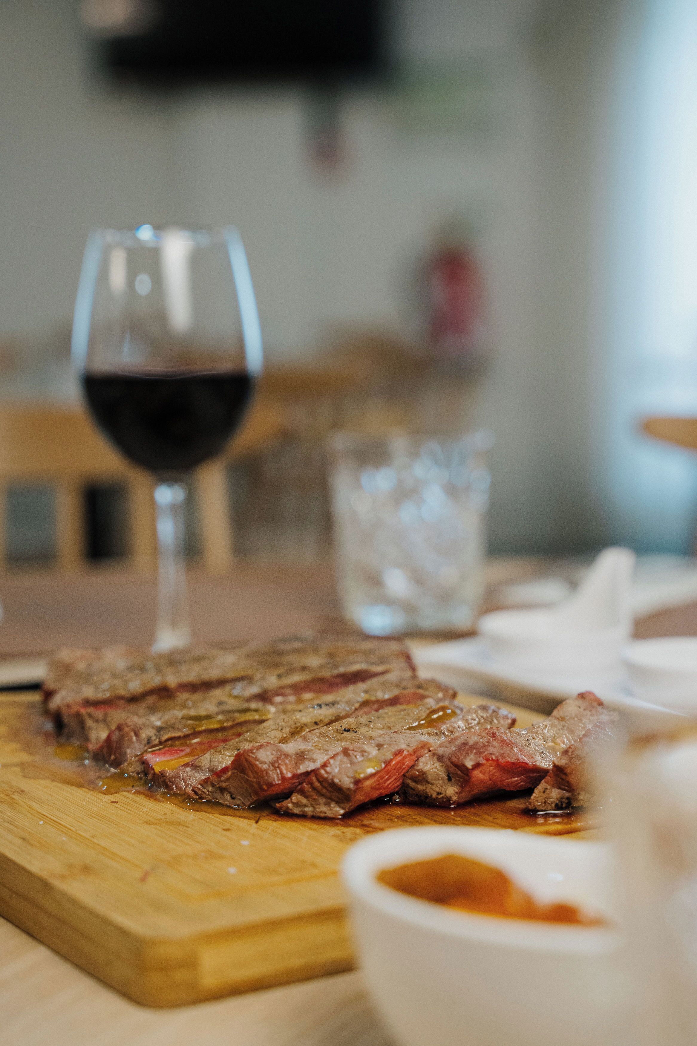 A steak on a wooden cutting board with a glass of red wine and a glass of water on the table.