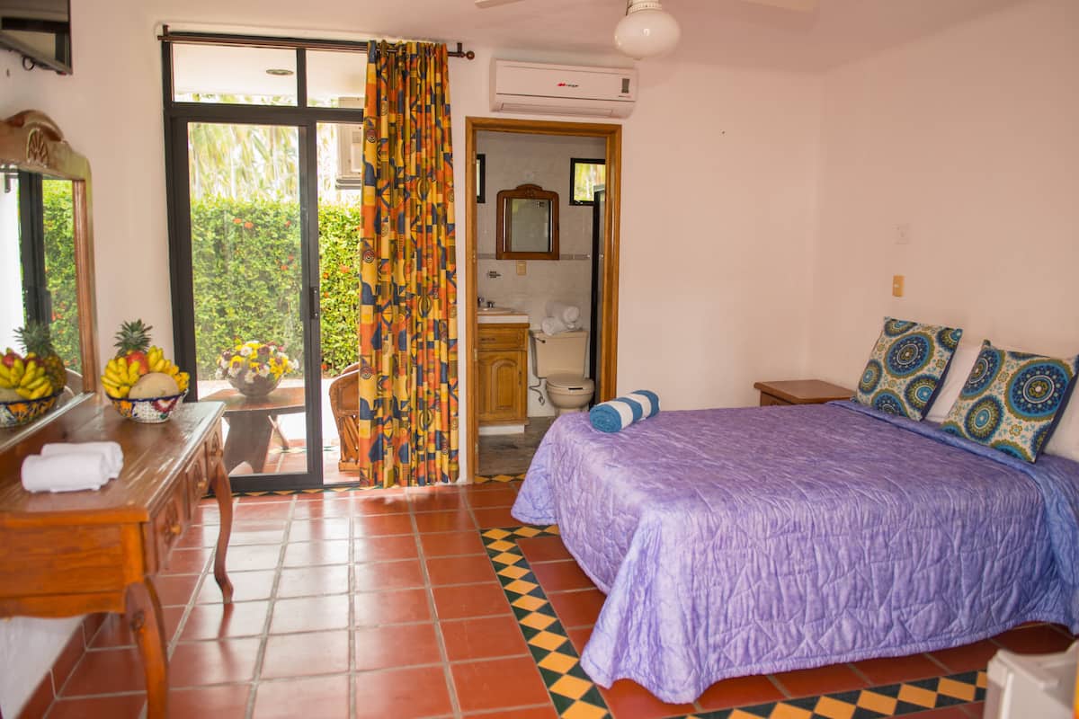 A bedroom with a bed, a dresser, a mirror, and a bathroom visible through an open door.