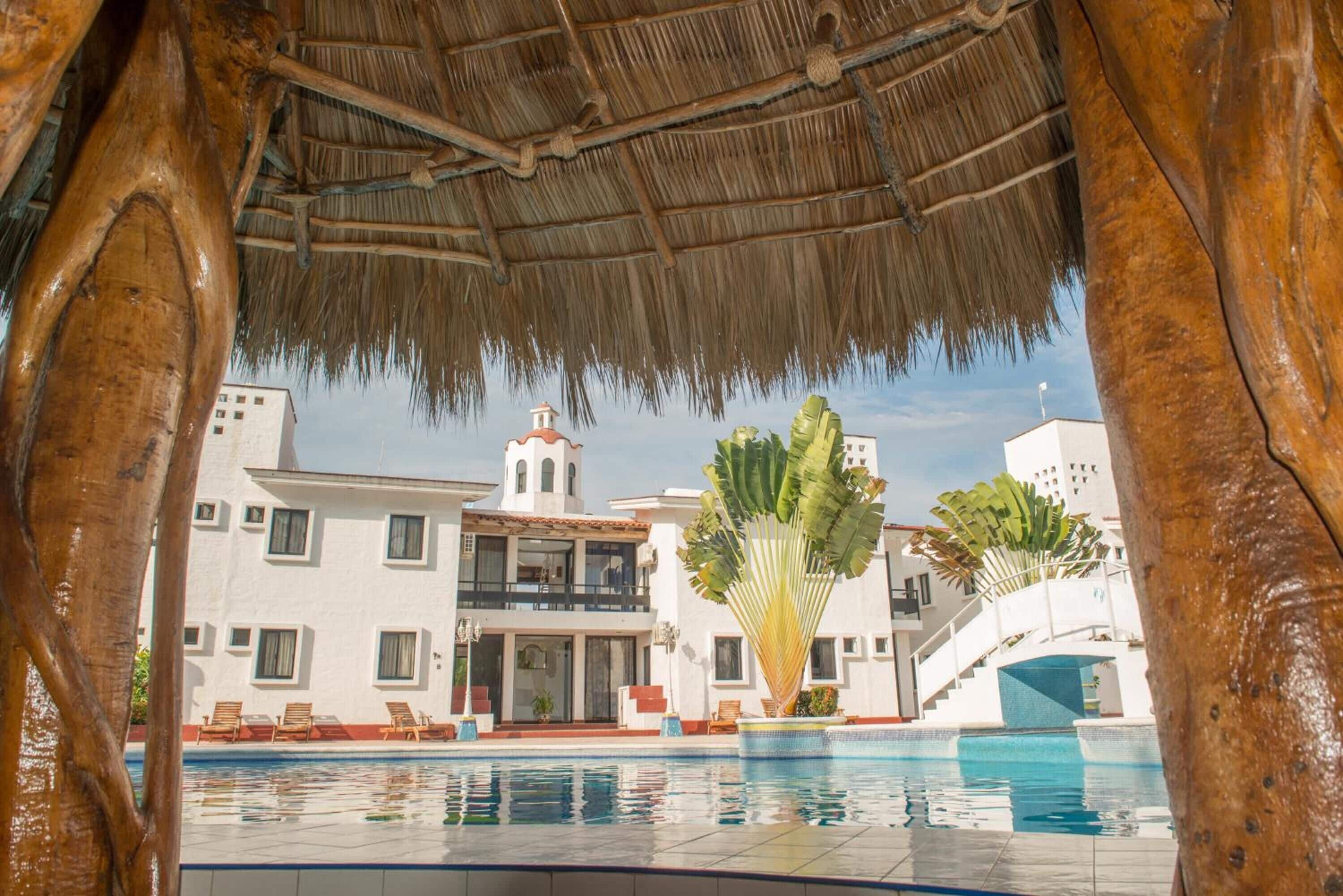 A pool area with a thatched roof, a white building with multiple floors, and a staircase leading to the upper levels.