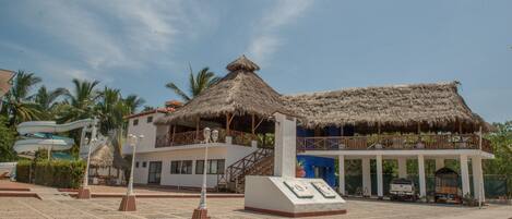 Ein Resort mit einem Gebäude mit Strohdach, einem überdachten Poolbereich und einem Sandstrand.
