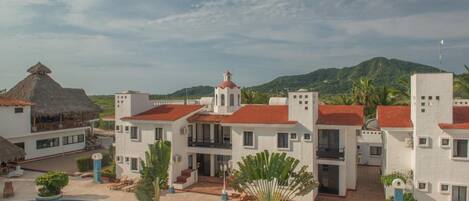 Un resort con piscina, edificios blancos de techos rojos y una montaña al fondo.