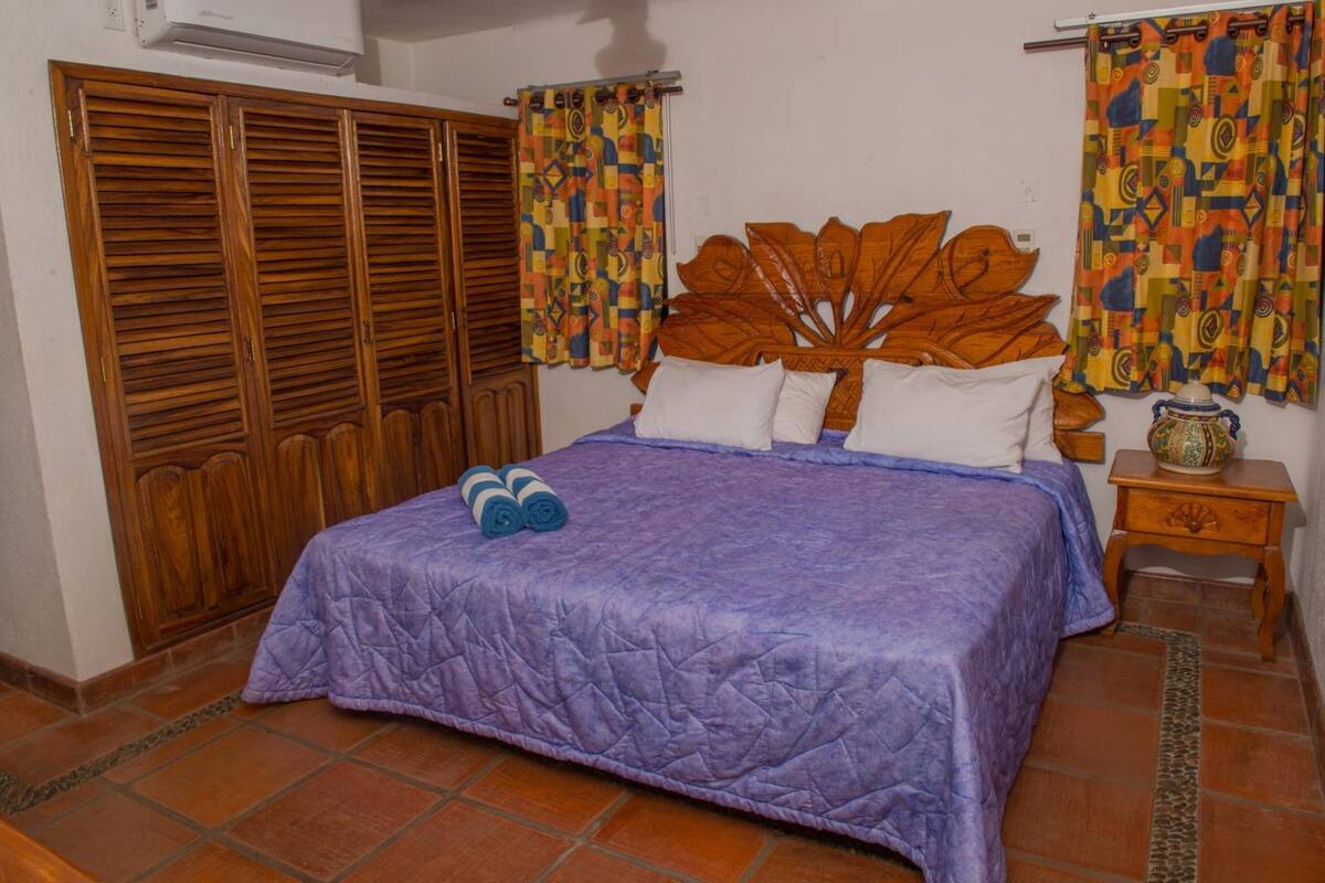 A bedroom with a wooden headboard, a purple bedspread, and a wooden wardrobe.