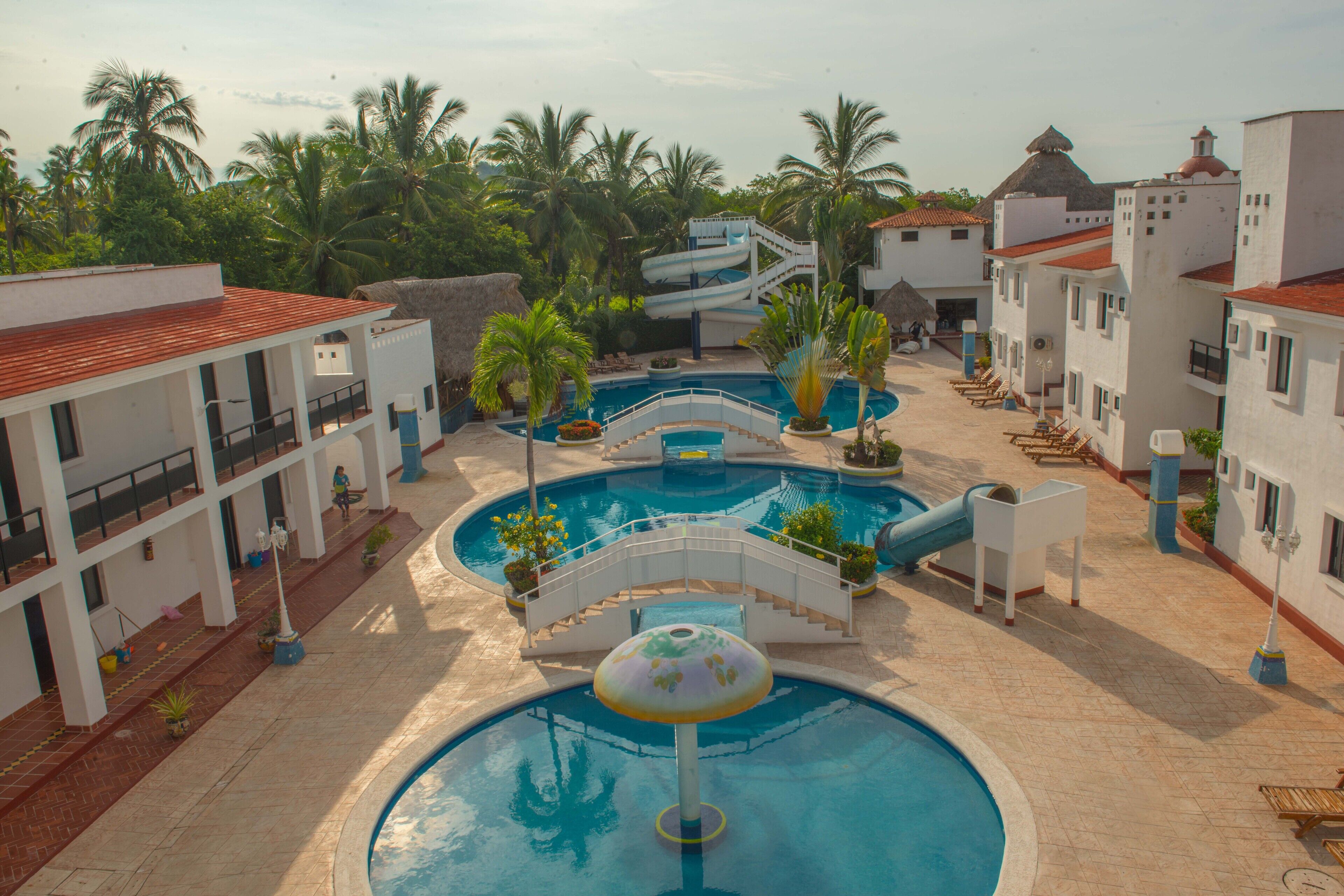 A resort with multiple swimming pools, palm trees, and a thatched-roof building.