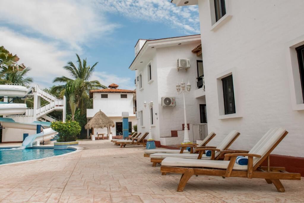 Un espace aménagé au bord de la piscine, avec des chaises longues, une piscine et un bâtiment à la façade blanche et aux ornements rouges.
