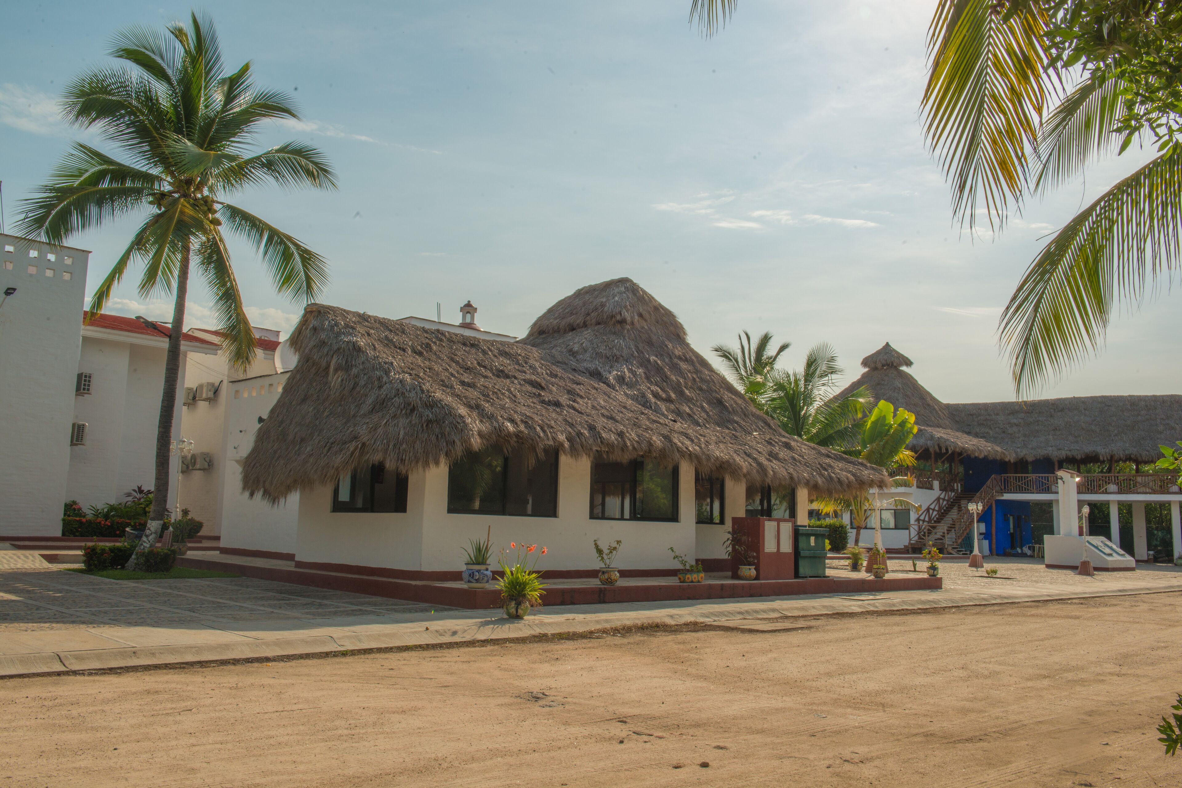 A building with a thatched roof, surrounded by palm trees and a clear sky.