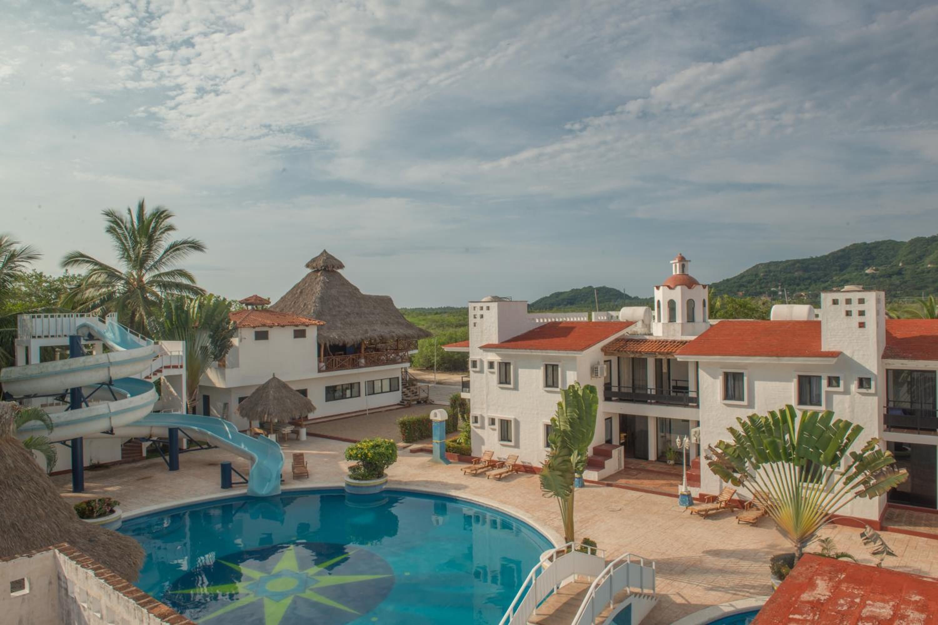 A resort with a swimming pool, a water slide, and thatched-roof structures.