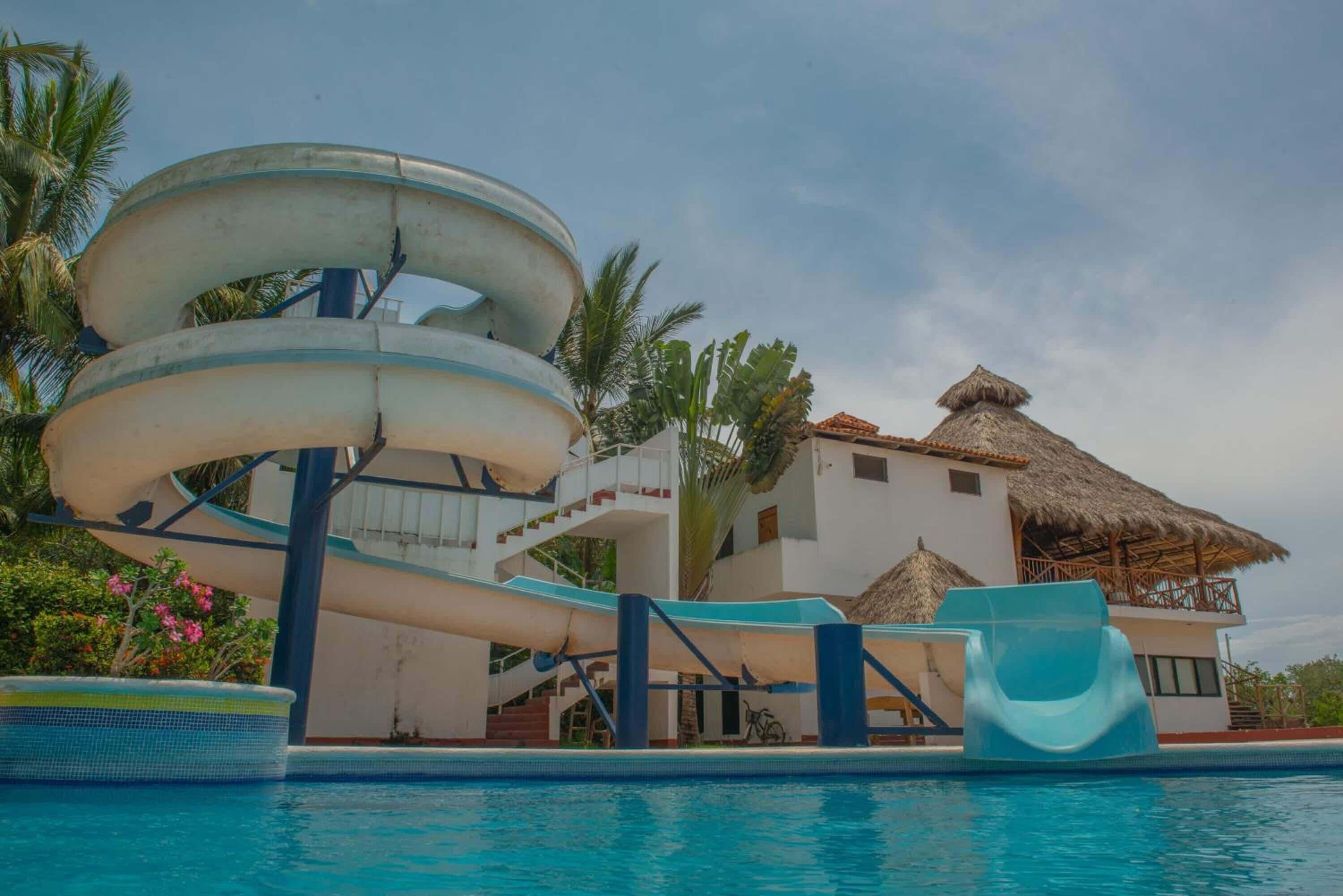 Un área de piscina con un tobogán y un edificio con techo de paja.