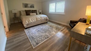 Une chambre à coucher comprenant un lit, des tables de chevet, un tapis, une fenêtre avec des stores et un bureau avec une lampe.