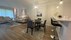 Un salon moderne comprenant un coin repas, un ensemble de canapés, une table basse et un bar avec des tabourets.