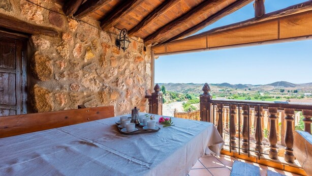 A stone-walled room with a balcony overlooking a mountainous landscape.