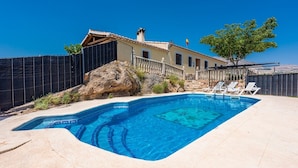 A swimming pool with a tiled edge, a stone wall, and a building with a tiled roof in the background.