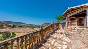 A stone pathway leading to a building with a wooden balcony overlooking a rural landscape with fields and mountains.