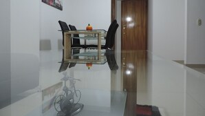Un comedor moderno con una mesa de vidrio, sillas negras y una puerta de madera al fondo.
