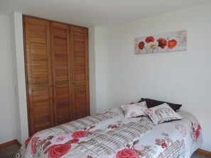 Quarto com cama, guarda-roupa de madeira e pintura floral na parede.