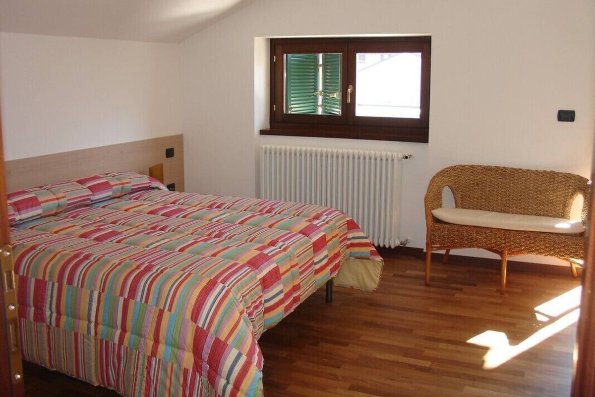 A bedroom with a bed, a window, a radiator, and a wicker chair.