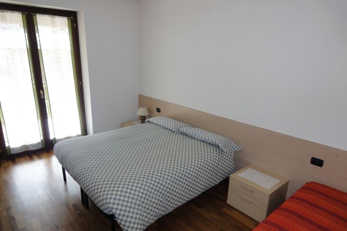 A bedroom with a bed, a nightstand, a lamp, and a box on the floor.