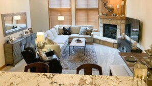 A living room with a fireplace, a sofa, a coffee table, and a dining area with a marble table. - TRUE Ski-In Ski-Out Luxury 2 bd. 2 bth -Riverbend Lodge -Perfect location! (Breckenridge)