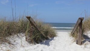 Un sentier de sable qui longe la plage et mène à l’océan, avec des poteaux en bois de chaque côté.