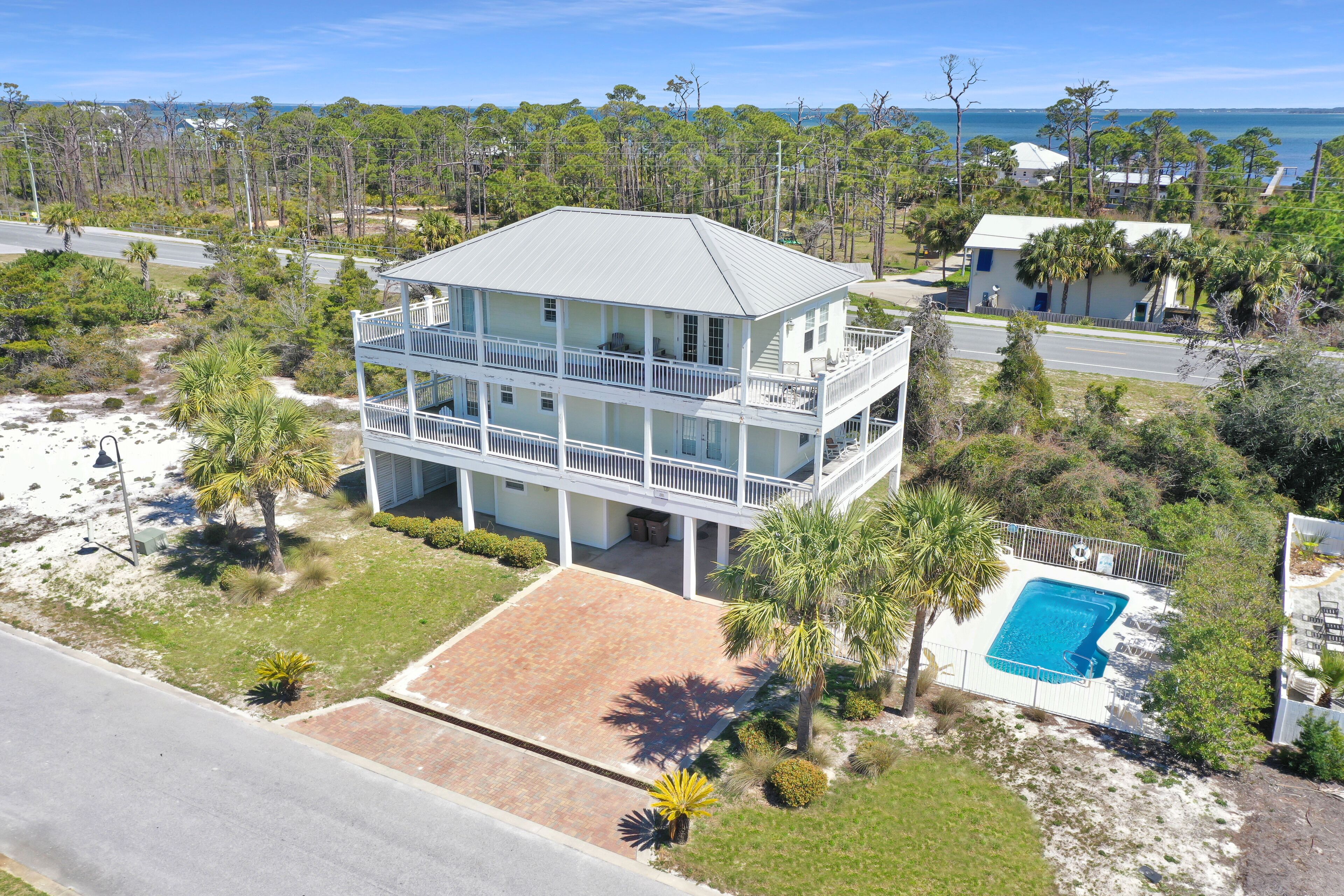A two-story beachfront house with a balcony, a swimming pool, and a view of the ocean.