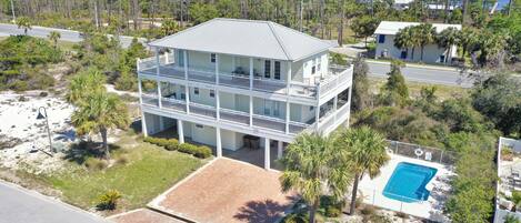 A two-story beachfront house with a balcony, a swimming pool, and a view of the ocean.