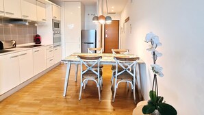 Une cuisine moderne avec des meubles blancs, une table à manger en bois et des chaises. On y trouve un réfrigérateur, un four et un four à micro-ondes.