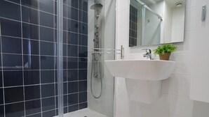 A modern bathroom with a glass-enclosed shower, a white sink with a mirror above it, and a small potted plant on the sink. - Apartment in Europe Square (Hospitalet de Llobregat)