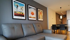 A modern living room with a grey sectional sofa, a dining area with a table and chairs, and three framed artworks on the wall. - Apartment in Europe Square (Hospitalet de Llobregat)