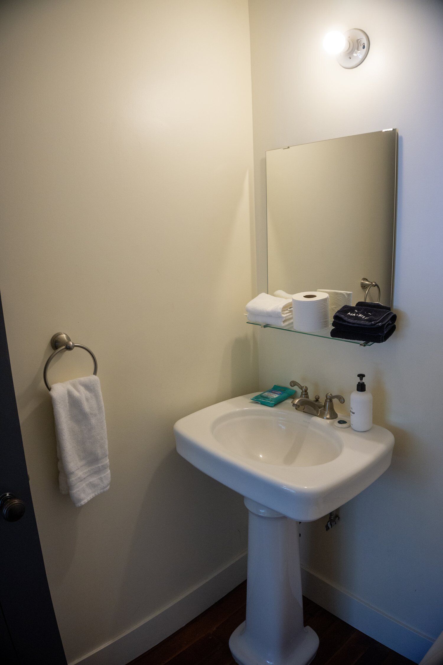 Une salle de bain avec un lavabo blanc, un miroir, un porte-serviettes et une étagère contenant des articles de toilette.