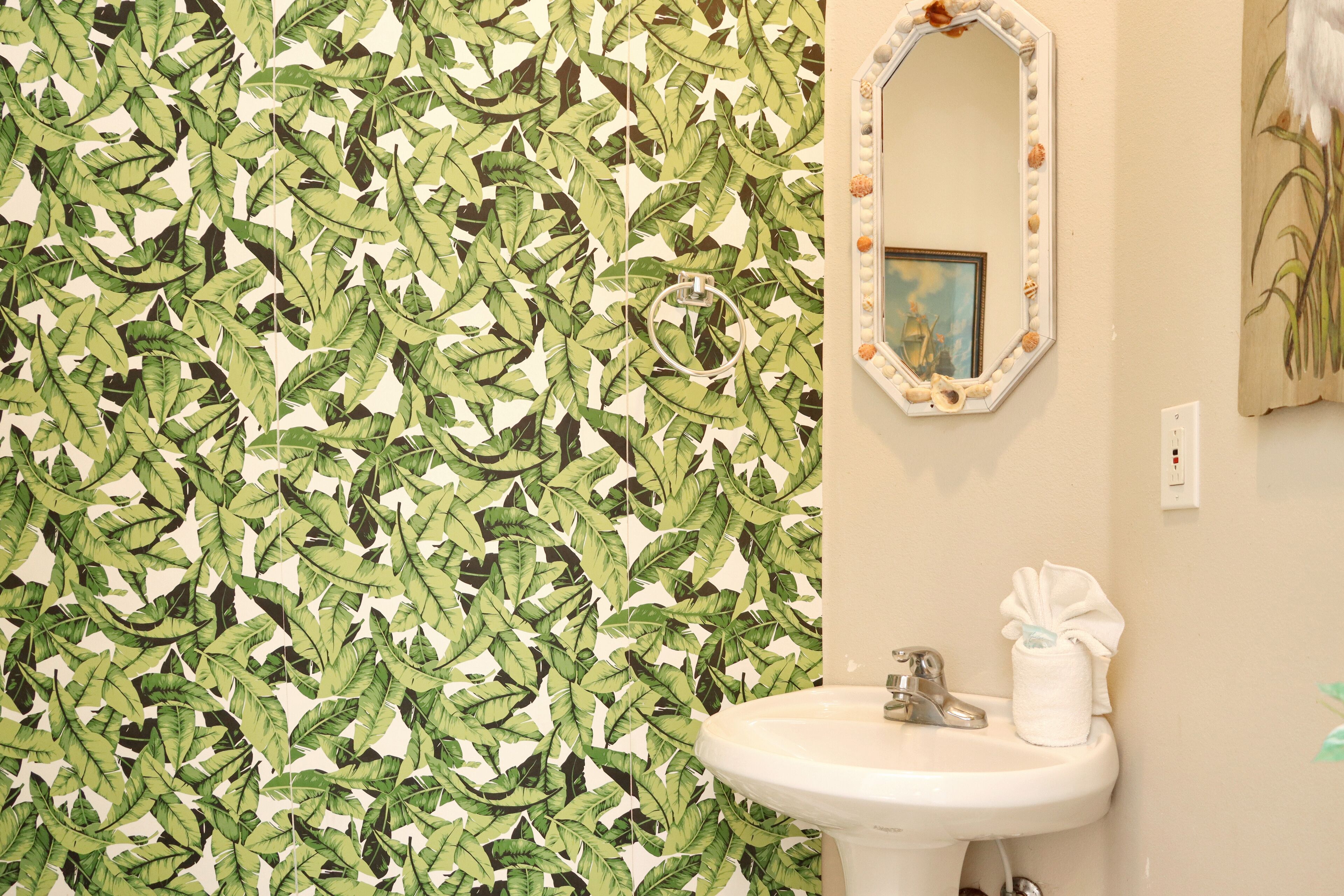 A bathroom with a leaf-patterned wallpaper, a white sink, and a mirror with a decorative frame.