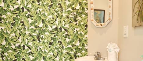 A bathroom with a leaf-patterned wallpaper, a white sink, and a mirror with a decorative frame.