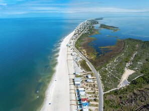 An aerial view of a coastal area with a beach, a road, and scattered buildings.