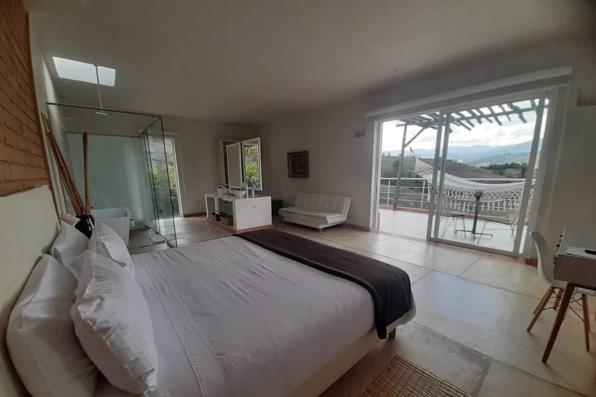A bedroom with a bed, a sofa, a small table, and a balcony with a view.